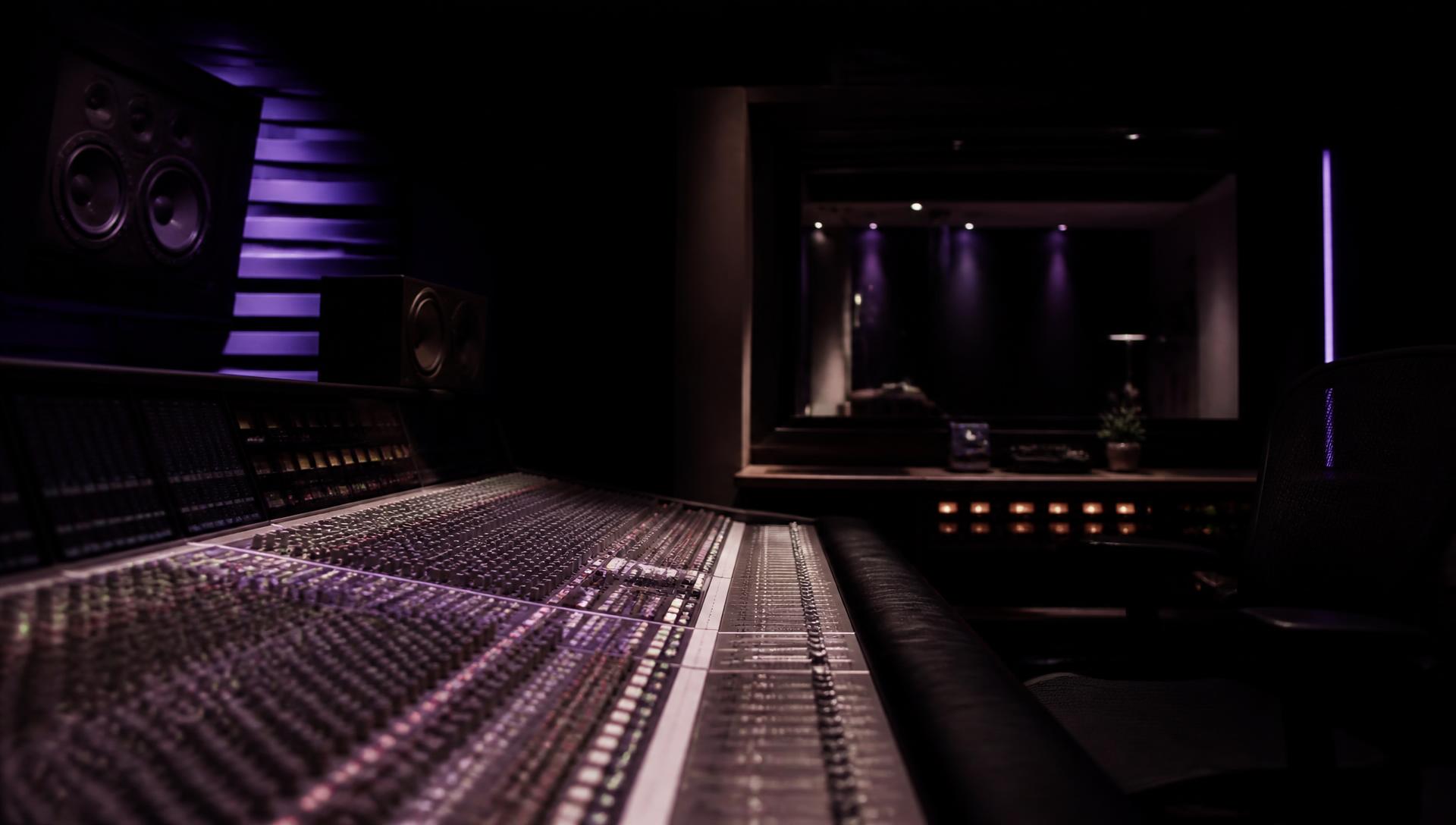 Large-format mixing console lit in violet inside the studio control room